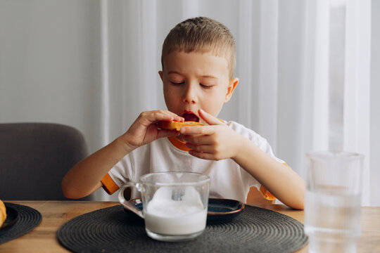 Boy enjoys snack at home while drinking milk in the morning light