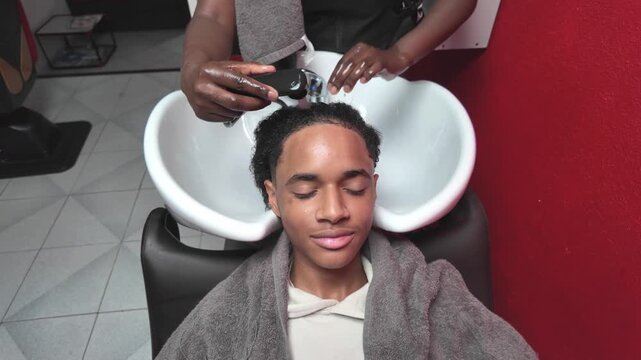 Teen boy sitting at salon sink getting his afro hair washed by a stylist