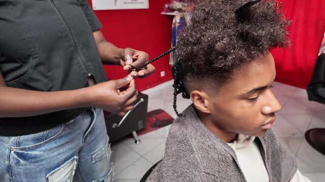 Side view of teen boy getting a braid done on the back of his afro hair by a stylist