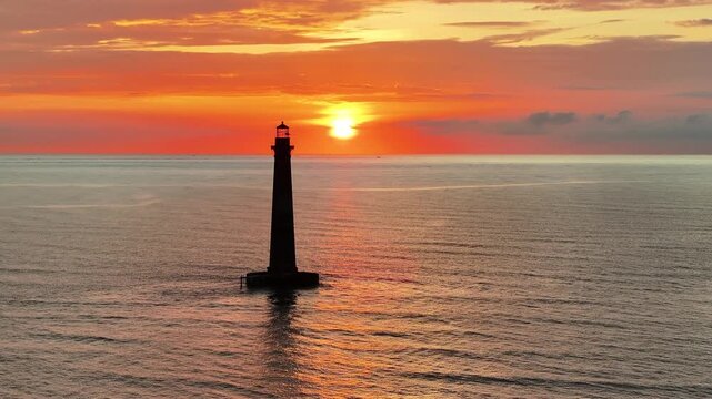 Cinematic aerial view of Morris Island Lighthouse and morning colorful orange sun along ocean horizon on Folly Beach near Charleston, South Carolina landscape seascape during sunrise - 4K Drone