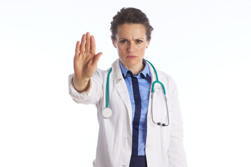 Fototapeta premium A professional female physician in a lab coat displays a serious expression and a stop hand gesture, conveying a medical warning, prohibition, or health advice.