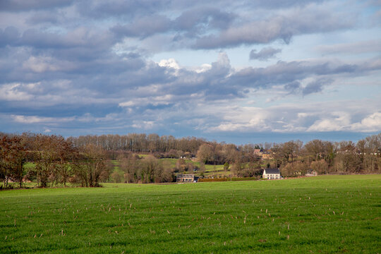 A farm field leading up to lone houses under a dramatic sky.