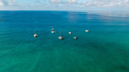 Aerial view of boats anchored in calm turquoise ocean water under a clear sky, tropical seascape with open horizon. © Bpato Media