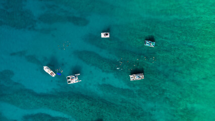 Aerial top down view of snorkeling tour boats anchored over shallow coral reef with people swimming in clear turquoise tropical ocean water. © Bpato Media