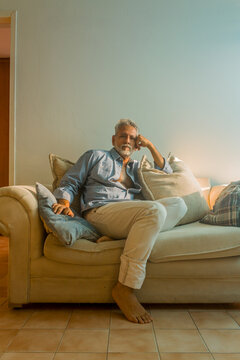 Stylish mature man with silver hair relaxing on a sofa in a bright living room