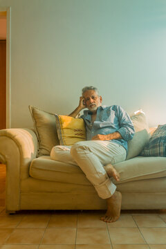 Stylish mature man with silver hair relaxing on a sofa in a bright living room
