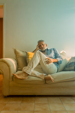 Stylish mature man with silver hair relaxing on a sofa in a bright living room