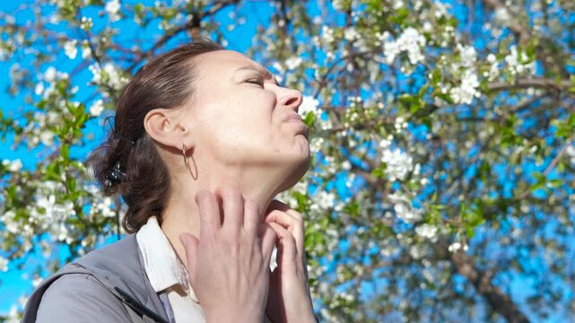 Female scratching inflamed areas. view of female with allergy inflammation scratching her skin by the flowers in the garden in the sun light