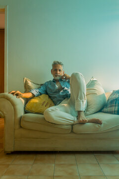 Stylish mature man with silver hair relaxing on a sofa in a bright living room