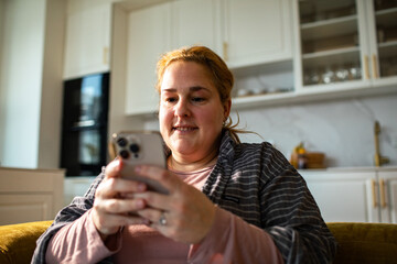 Fototapeta premium Smiling woman using smartphone in modern home kitchen