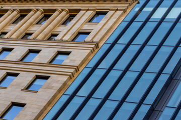 Close-up diagonal composition of heritage sandstone building meeting sleek modern glass facade, contrasting warm masonry details with cool reflective panels in urban cityscape. © Alex