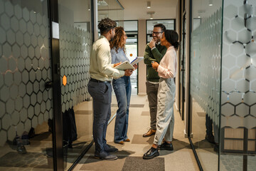 Diverse business colleagues discussing ideas in office hallway