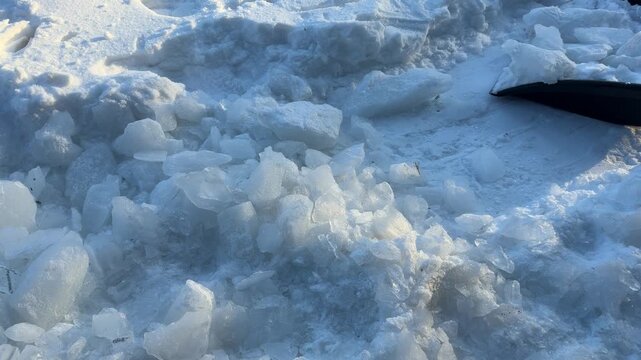 Pile of Broken Ice Chunks with Shovel. A close-up shows a pile of large translucent ice chunks near a heat pump, with a black shovel visible from snow clearing.