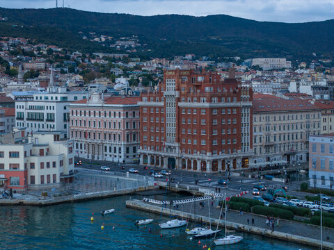 Aerial view of the grand, red-brick Generali Group Academy casting its regal presence over the bustling port and shimmering waters, Trieste, Italy.