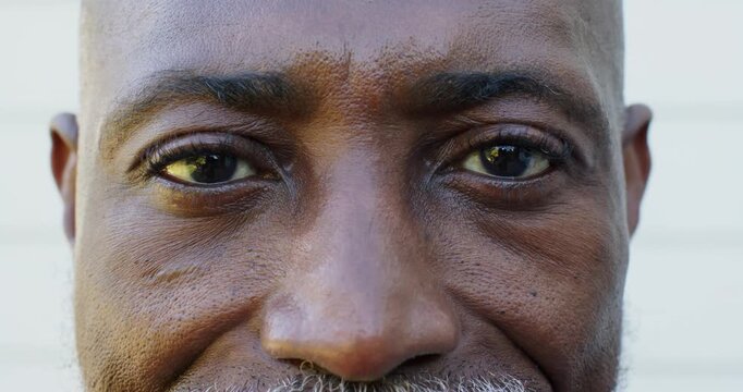 Senior African American man holding gaze, smiling, engaging camera as frame pulling back by siding