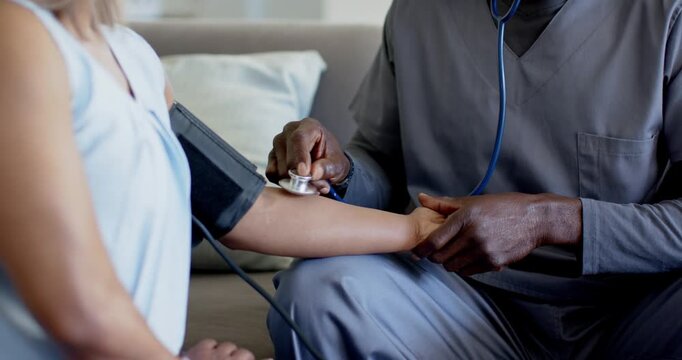 Provider checking BP on patient at home for routine check, holding cuff and wrist with stethoscope