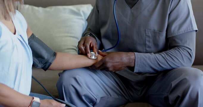 Clinician listening on sofa, adjusting blue stethoscope on patient arm cuff, checking BP and pulse