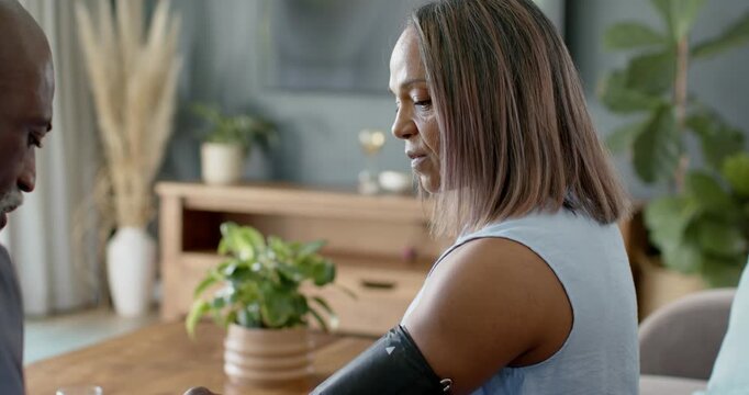 African American caregiver prompted by concern placing BP cuff on woman at table, checking watch