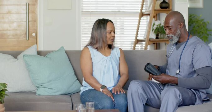 African American nurse opening kit, applying BP cuff on patient at home, showing tablet results
