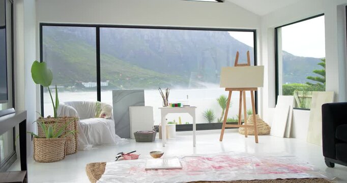 Camera panning slowly, revealing art studio with wooden easel, paints and rug showing workspace