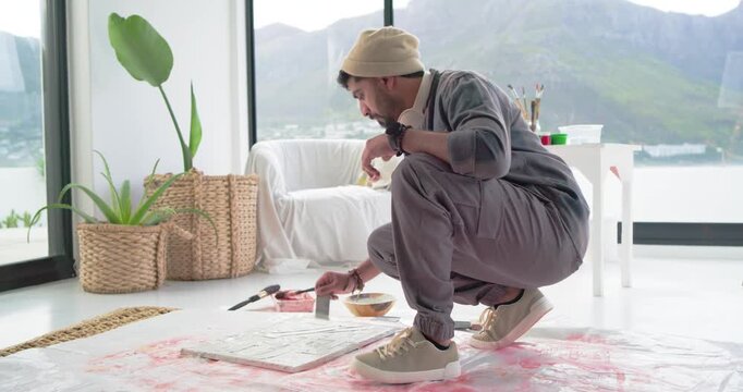 Artist is dipping palette knife, scraping and brushing floor canvas by window, refining composition