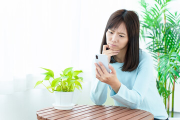 困った顔をしてスマートフォンを使う女性