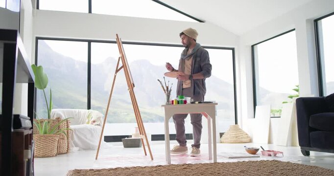 Indian man rising toward easel, mixing paints, painting canvas to create art in studio