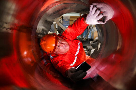 Industrial worker inspecting inside large metal pipe during maintenance work