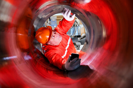 Industrial worker inspecting inside large metal pipe during maintenance work