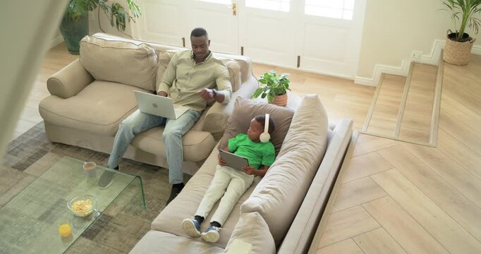 Man and schoolboy pausing laptop tapping shoulder for notice fixing headset back to tablet at home