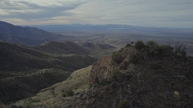 Aerial orbit of two men on a desert mountain summit