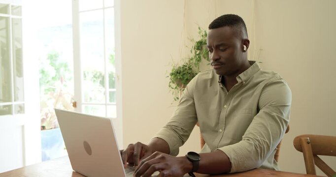 African American man in olive shirt working on laptop at home, glancing toward glass door, smiling