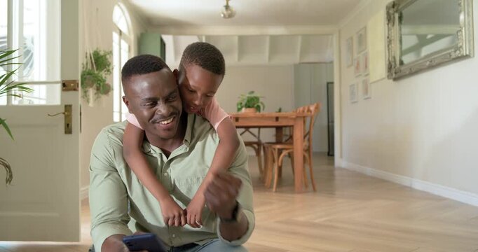 African American dad and son playing on step, child climbing on dad's back, dad holding phone