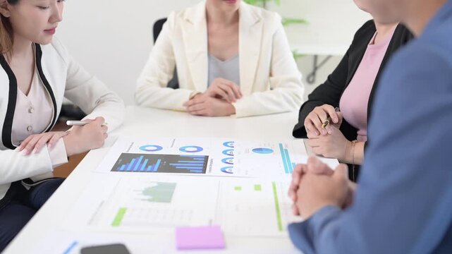 A group of people are sitting around a table with a large graph on it. They are discussing the graph and its implications