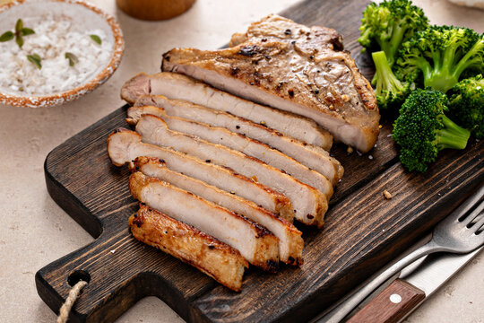 Pork chop grilled or sauteed sliced on a cutting board with broccoli