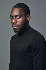 Fototapeta premium African man portrait in creative conceptual visual style wearing black turtleneck sweater with serious expression on gray background. Studio lighting highlights skin texture and facial features.