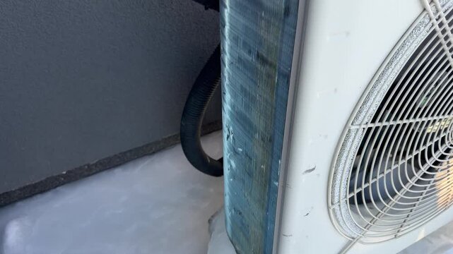 Ice Encasing the Side of a Heat Pump Unit. A high-angle close-up displays a heat pump side panel frozen over with ice at the base, with snow texture indicating prolonged cold.