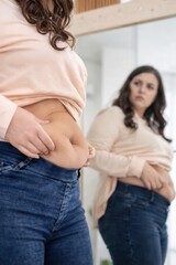 Young woman examining her body in mirror, body positivity concept