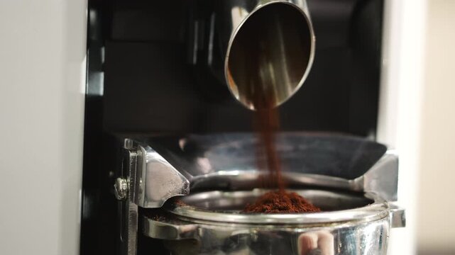 Ground coffee pouring into a portafilter of an espresso machine, close up coffee preparation process, barista workflow and professional coffee brewing indoors.