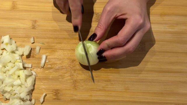 Dicing an Onion on a Wooden Cutting Board Close Up. A close-up shows hands dicing a white onion on a wooden board, pushing chopped pieces aside to reveal the onion&rsquo;s crisp, layered texture.