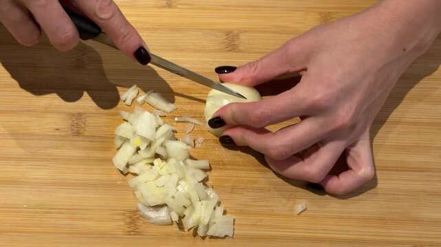 Finely Dicing a White Onion on a Wooden Board. A top-down video shows hands finely dicing an onion on a wooden board, gathering the chopped pieces into a neat pile with a knife.