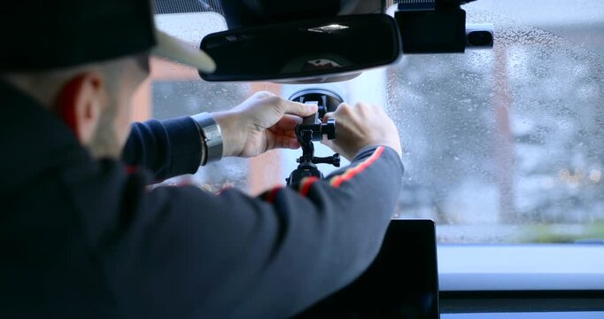 A person is attaching an action camera to a car windscreen using a suction mount.