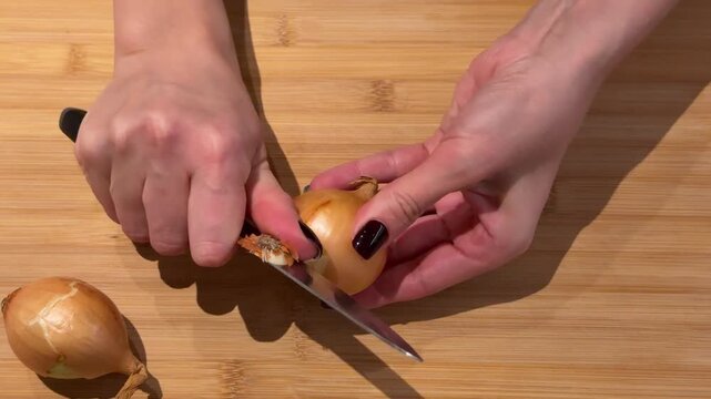 Peeling and Cleaning a Whole Onion on a Cutting Board. A close-up captures hands carefully peeling and cleaning a white onion on a wooden board, removing dry layers to reveal the fresh bulb.