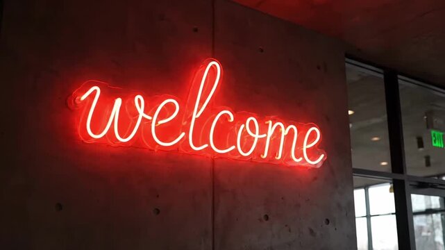 Neon welcome sign on a concrete wall near a glass door.