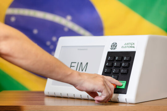 Urna eletr&ocirc;nica brasileira durante elei&ccedil;&otilde;es presidenciais, com eleitor pressionando o bot&atilde;o confirmar. Conceito de democracia, dever c&iacute;vico e processo eleitoral no Brasil.