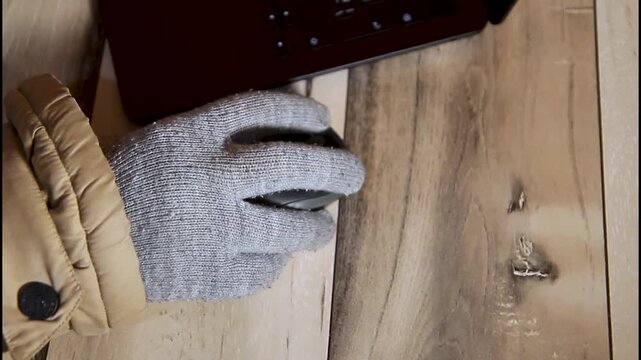 Close up side view of a hand in a warm glove using a computer mouse during winter blackout in Ukraine, showing remote work and cold indoor conditions.
