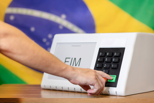 Urna eletr&ocirc;nica brasileira durante elei&ccedil;&otilde;es presidenciais, com eleitor pressionando o bot&atilde;o confirmar. Conceito de democracia, dever c&iacute;vico e processo eleitoral no Brasil.