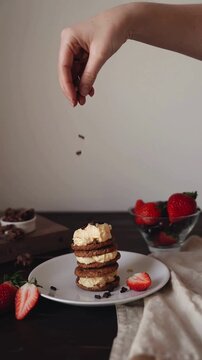 Woman Hand Sprinkling Chocolate Nibs on Oatmeal Cookie Sandwich Tower with Cream Filling