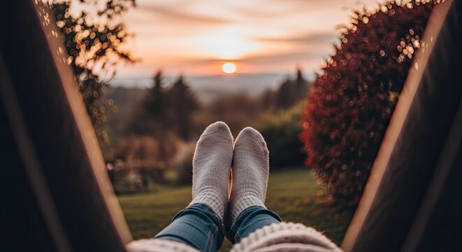 Person's feet in cozy socks on a window seat, overlooking a serene garden at sunset.