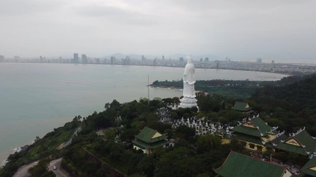 Giant white lady buddha statue overlooks ocean and danang city skyline.